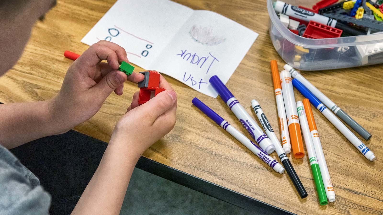 小孩子在桌上用马克笔和填色纸玩乐高玩具